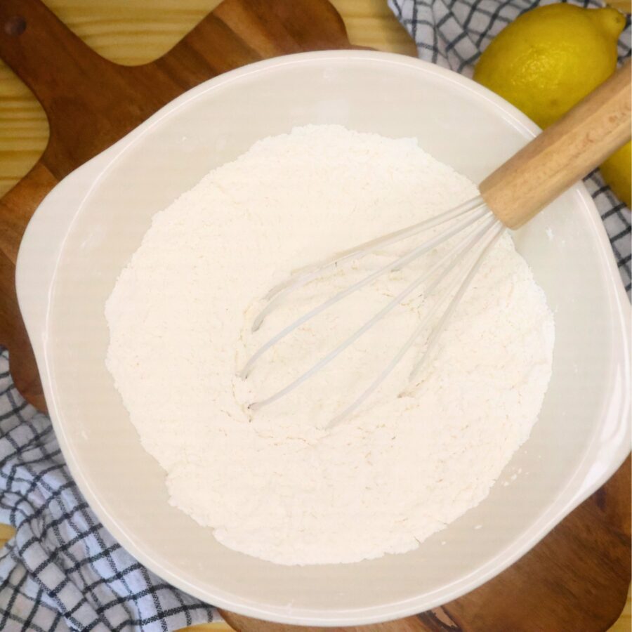Dry ingredients for lemon muffins in a mixing bowl with a whisk