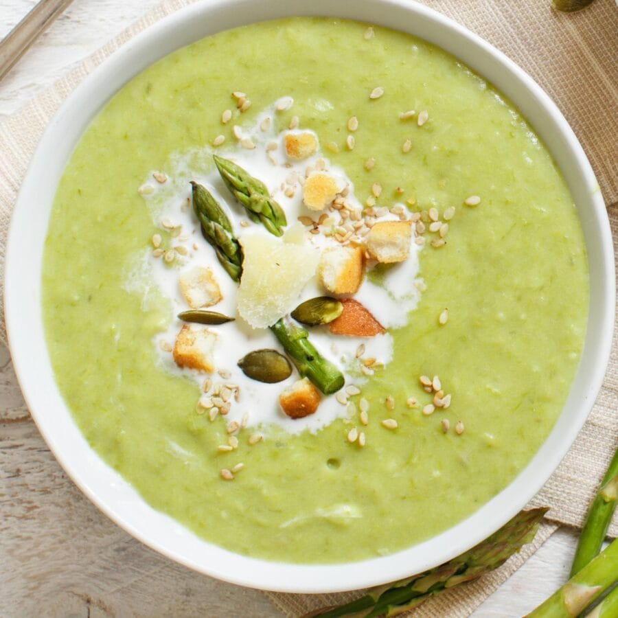 Close up image of a white bowl full of Asparagus Soup with garnish