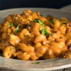 A serving of Cheeseburger Mac on a white plate with a parsley garnish