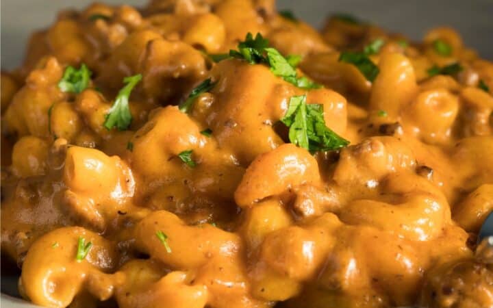A serving of Cheeseburger Mac on a white plate with a parsley garnish