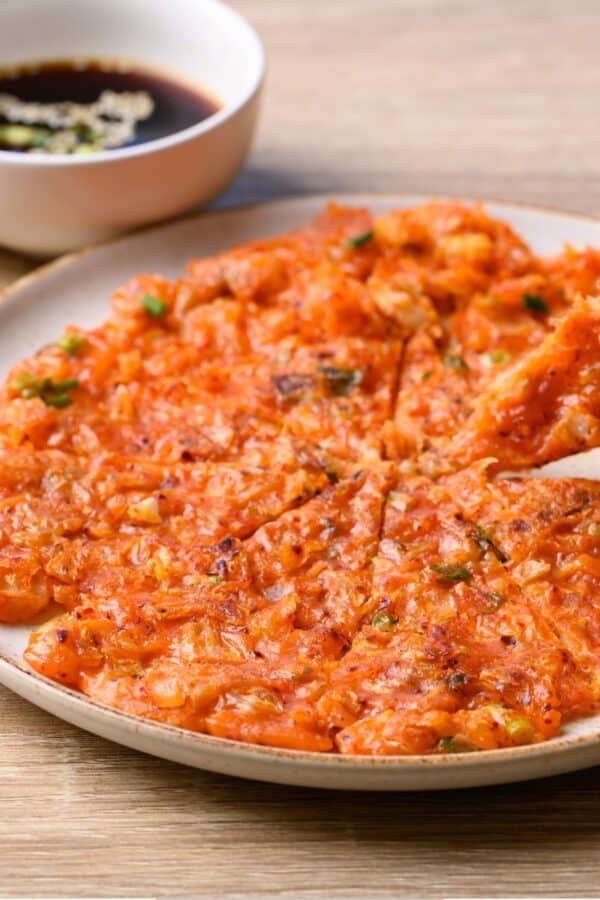 A Kimchi Pancake on a white plate being eaten with chopsticks