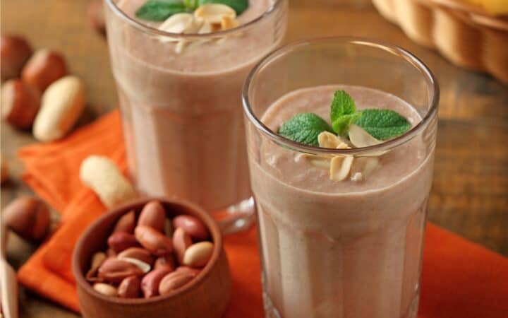 Two Protein Smoothies in glasses next to peanuts and bananas