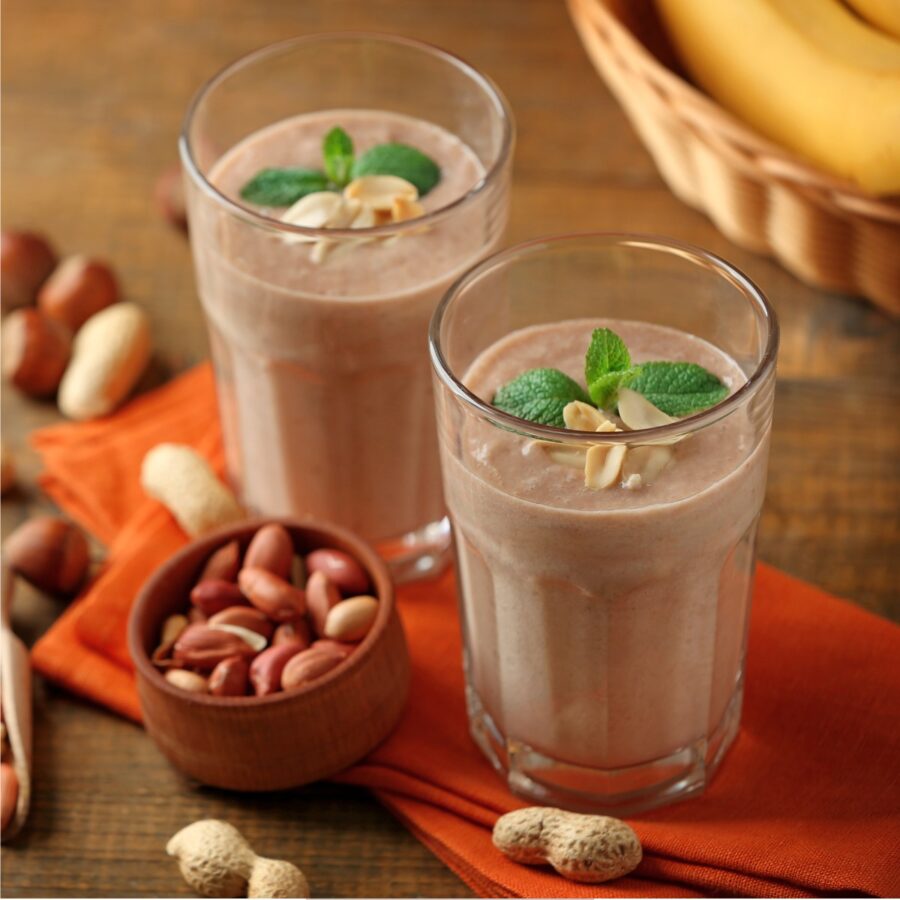 Two Protein Smoothies in glasses next to peanuts and bananas