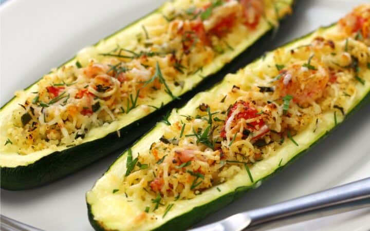 Two Zucchini Boats on a white plate with silverware