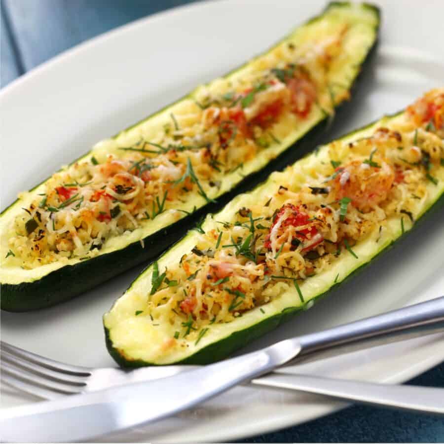 Two Zucchini Boats on a white plate with silverware