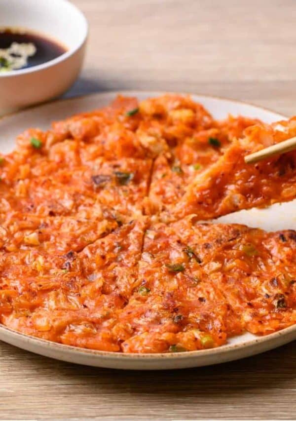 A Kimchi Pancake on a white plate being eaten with chopsticks