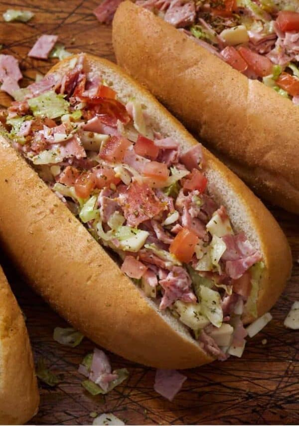 Overhead image of an Italian Chopped Sandwich next to two more sandwiches on a wooden surface