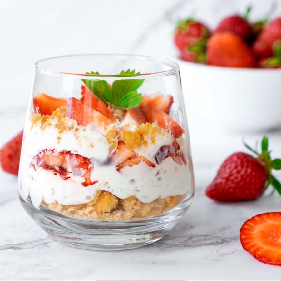 A single serving Strawberry Trifle in a glass bowl with strawberries surrounding it