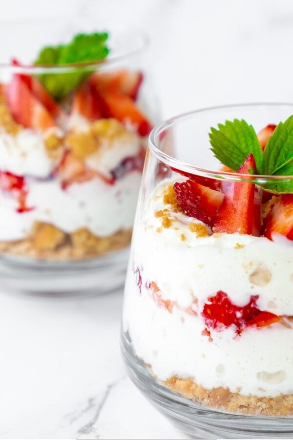 Two small Strawberry Trifles in glass cups on a white surface