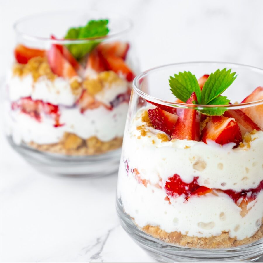 Two small Strawberry Trifles in glass cups on a white surface
