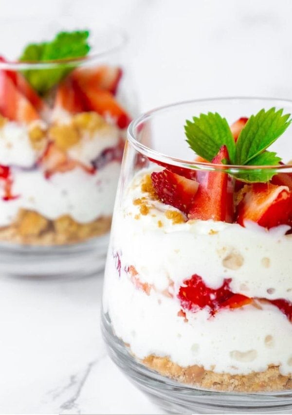 Two small Strawberry Trifles in glass cups on a white surface