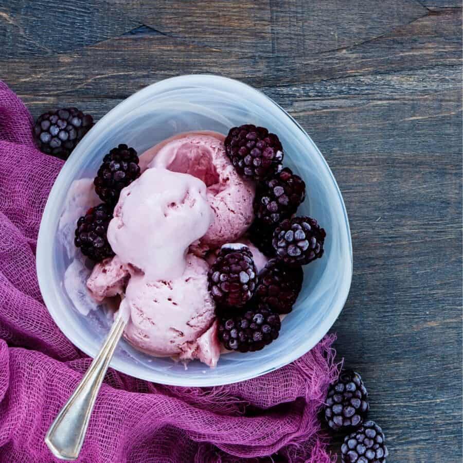 A bowl of homemade blackberry ice cream in a whole with a spoon