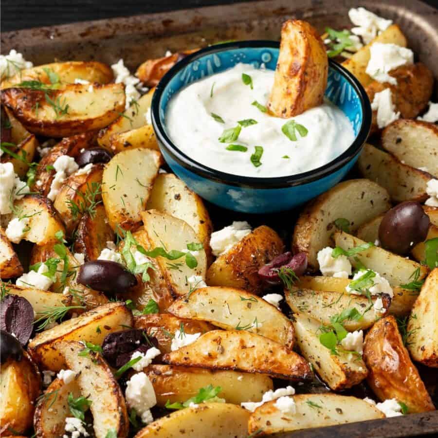 Greek Potatoes on a pan with a bowl of dipping sauce