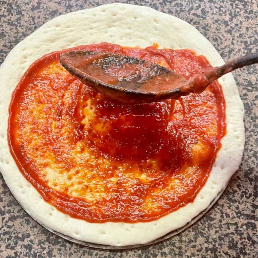 Homemade Pizza Sauce being spread on pizza dough with a large spoon