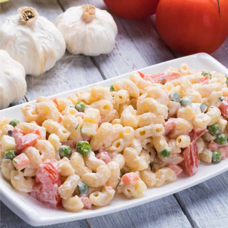 Close up image of Macaroni Salad on a white tray with veggies in the background