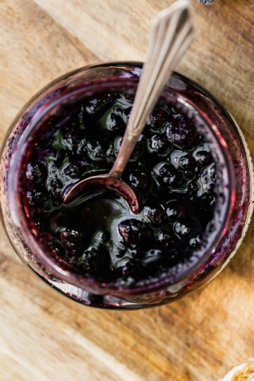 Overhead image of Blueberry Compote in a glass jar with a serving spoon
