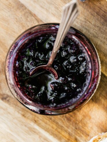 Overhead image of Blueberry Compote in a glass jar with a serving spoon