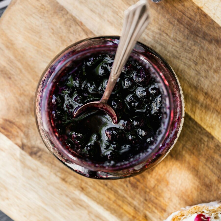 Overhead image of Blueberry Compote in a glass jar with a serving spoon