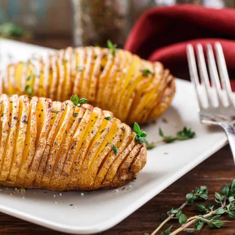 Close up image of Hasselback Potatoes on a white plate on a rustic surface
