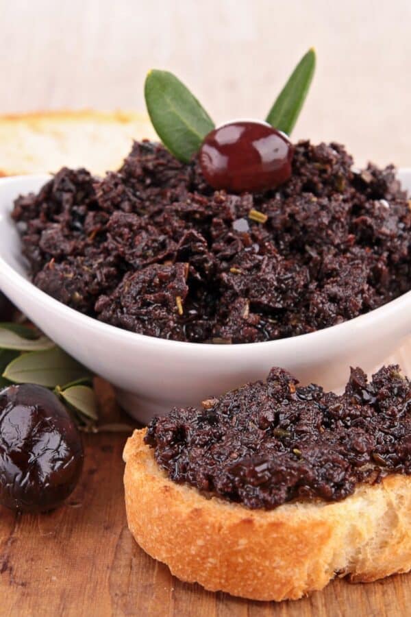 Olive Tapenade in a white bowl and spread on a piece of bread