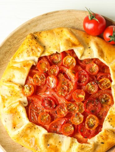A Tomato Galette on a neutral surface with fresh tomatoes next to it