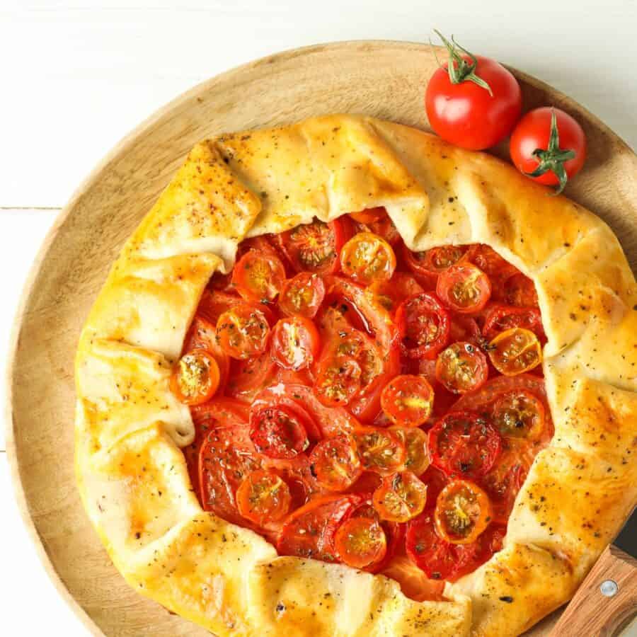 A Tomato Galette on a neutral surface with fresh tomatoes next to it
