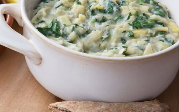 Close up image of Vegan Spinach Artichoke Dip in a white dish with flatbread pieces