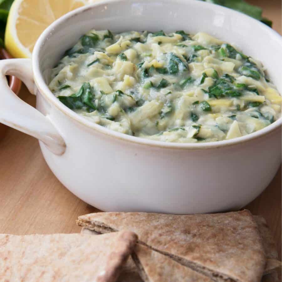Close up image of Vegan Spinach Artichoke Dip in a white dish with flatbread pieces
