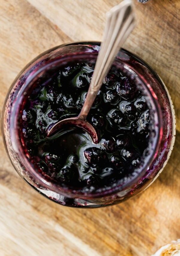 Overhead image of Blueberry Compote in a glass jar with a serving spoon