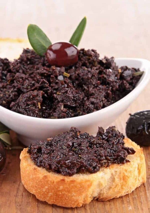 Olive Tapenade in a white bowl and spread on a piece of bread
