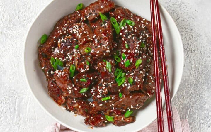 Overhead image of crispy beef in a white bowl with chopsticks