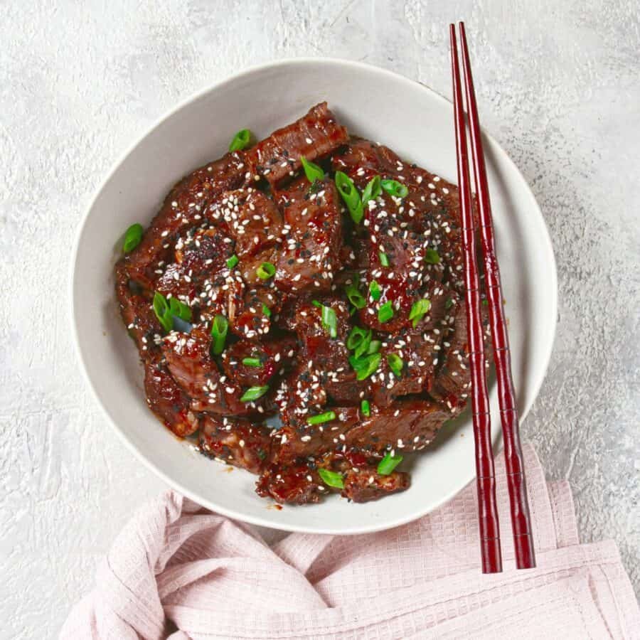 Overhead image of crispy beef in a white bowl with chopsticks