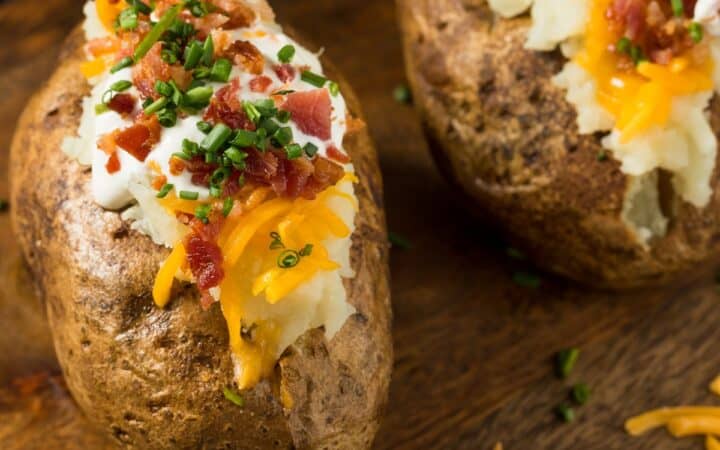 Two Jacket Potatoes with toppings on a wooden cutting board
