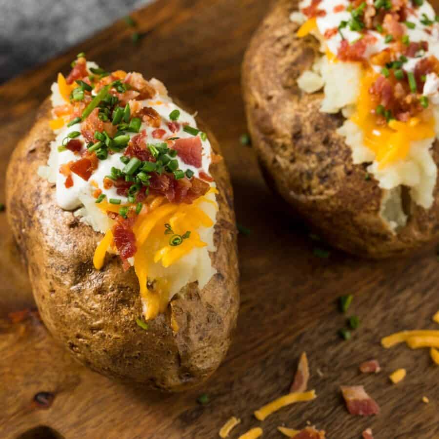 Two Jacket Potatoes with toppings on a wooden cutting board