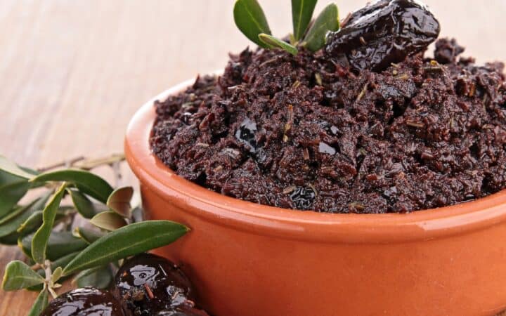 Homemade Olive Tapenade in a brown bowl with olives next to it