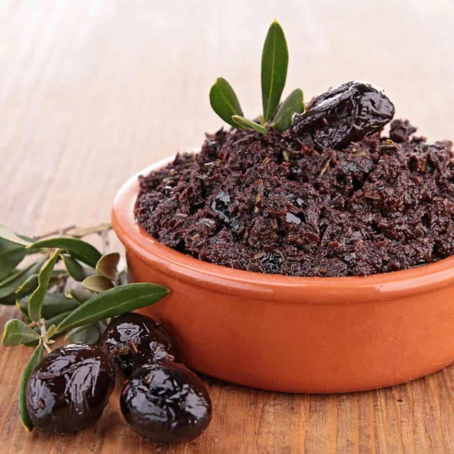 Homemade Olive Tapenade in a brown bowl with olives next to it