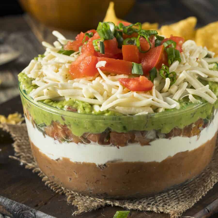 Close up image of Seven Layer Dip in a bowl on a rustic table