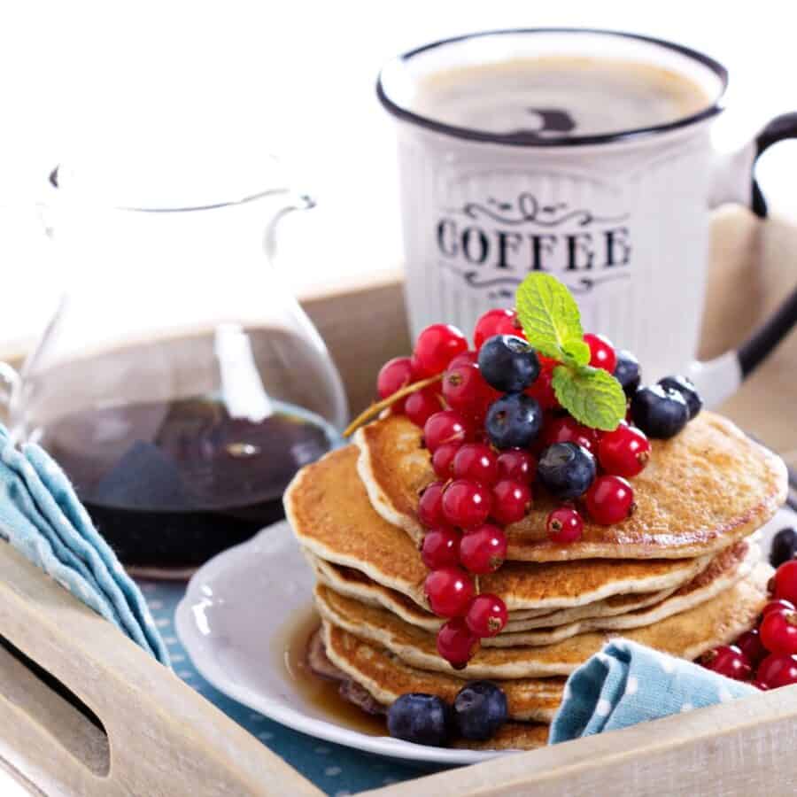 A stack of Vegan Pancakes on a plate with berries with a cup of coffee