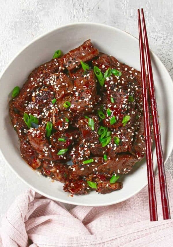 Overhead image of crispy beef in a white bowl with chopsticks