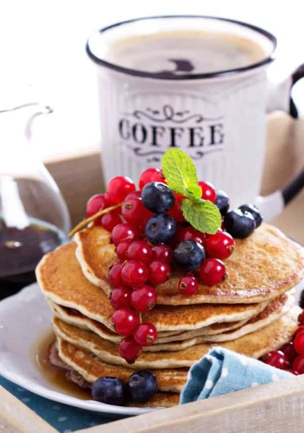 A stack of Vegan Pancakes on a plate with berries with a cup of coffee