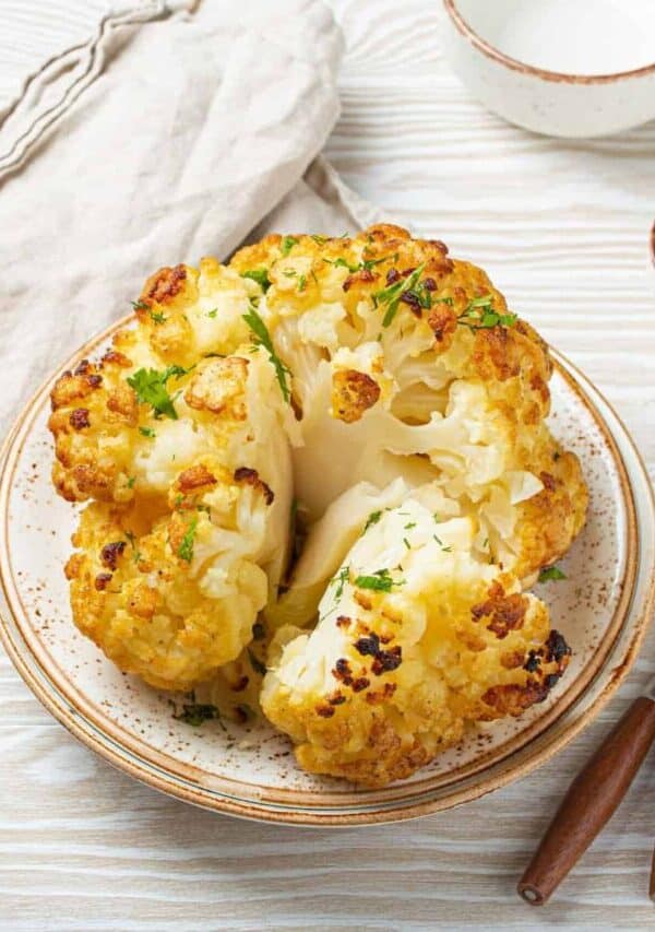 Overhead image of a Whole Roasted Cauliflower cut into pieces on a plate
