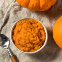 Overhead image of Pumpkin Puree in a white bowl next to pumpkins