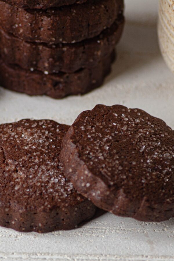 A stack of chocolate shortbread cookies with two laying in front of them