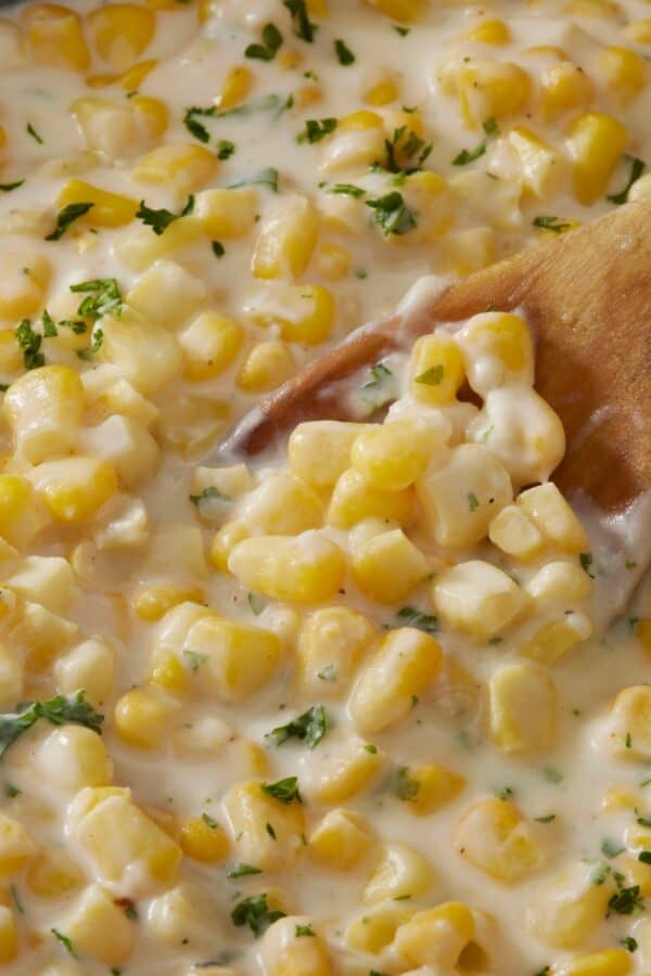 Overhead image of creamed corn in a skillet with a wooden spoon serving it