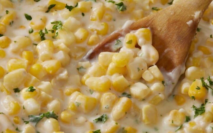Overhead image of creamed corn in a skillet with a wooden spoon serving it