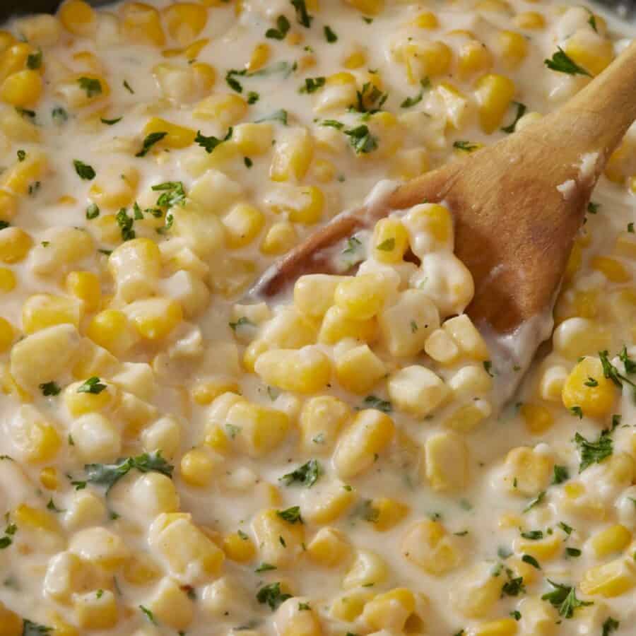 Overhead image of creamed corn in a skillet with a wooden spoon serving it