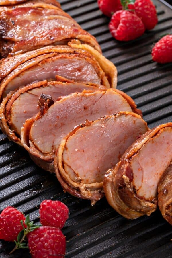 Close Up image of bacon wrapped pork tenderloin with raspberries next to it