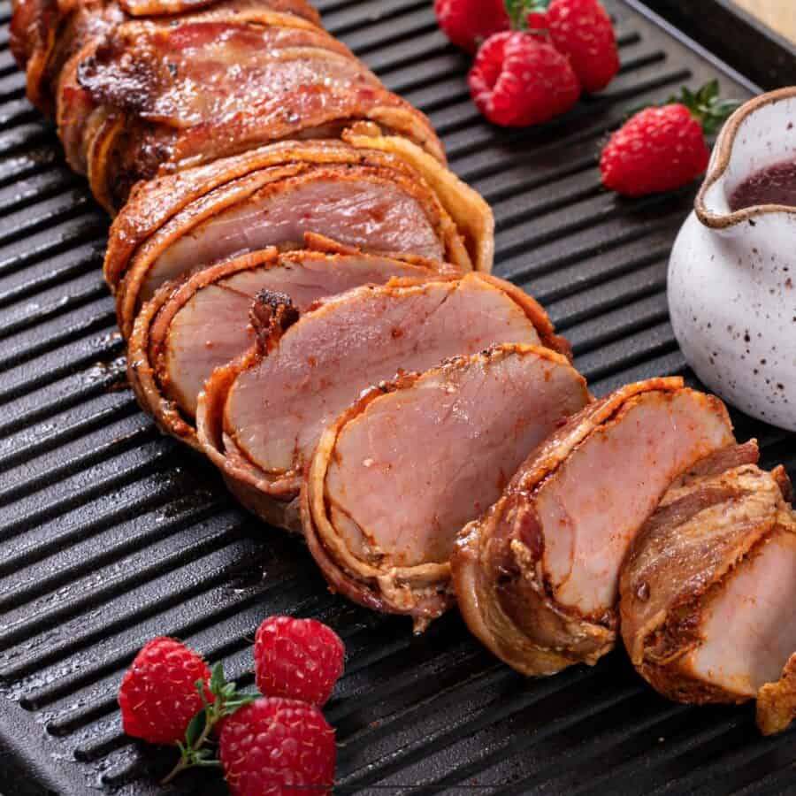 Close Up image of bacon wrapped pork tenderloin with raspberries next to it