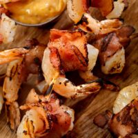 Bacon Wrapped Shrimp on a cutting board with a side of mustard