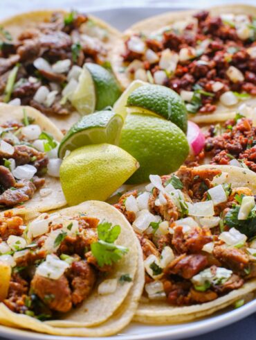 Overhead image of a variety of tacos on a plate with limes in the middle